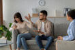© Prostock-studio - An angry couple discusses their relationship issues with a therapist. The man gestures expressively while the woman appears focused on her phone.