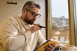 © Bliss - Handsome mature man enjoys coffee while recording thoughts in stylish cafe setting