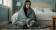 © Mauricio - Young asian woman wrapped in a cozy blanket sitting on the floor in bedroom