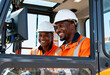 © Anna - Two smiling construction workers in a heavy machinery cab. Black male colleagues using a computer for on-the-job training. Teamwork and industrial technology concept