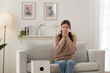 © surachetkhamsuk - Asian woman sneezing and using tissue while sitting on sofa at home with air purifier