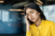 © Tetiana - Close-up photo of a young Indian woman in an office, holding her head in her hand and grimacing in pain