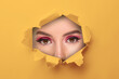 © New Africa - Young woman with beautiful makeup, closeup. View on eyes through torn hole in orange paper