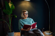 © okrasiuk - Middle aged woman reading book in scandy style hygge dark interior home. Lady dreaming, enjoy calm mood without stress, well being alone. Take a break and relax. Cozy holidays time at home.