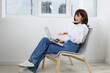 © SHOTPRIME STUDIO - Casual female professional sits in a bright, modern room, typing on a laptop with a relaxed posture. Soft light, airy space, and simple furnishings suggest productive work during a quiet day at home