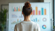 © Viktor - Rear view of woman looking at graphs on whiteboard. Businesswoman analyses data. Financial graphs shows success, growth. Strategy, planning concept. Teamwork, meeting, discussion in corporate office.