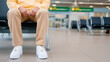 © MarGa - Person waiting for a flight in an airport departure lounge. Unrecognizable passenger sitting alone on a bench in a modern terminal. Travel concept with copy space