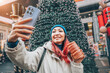 © EdNurg - Happy young woman taking selfie with a smartphone and authentic Trdelnik at snowy European Christmas market