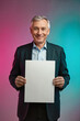 © f_bossa - A smiling mature man in a suit holding a blank white sign against a vibrant pink and blue gradient background.