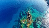 Aerial view of the ocean, displaying vibrant blues and turquoise over submerged rocks and a rocky coastline