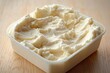 © Gzvzattio - creamy pale spread scooped in an open plastic tub on a wooden surface, smooth texture and inviting appearance