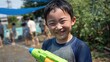 © mila103 - A young boy is happily engaged in a water gun fight during a summer gathering. Surrounded by friends, laughter fills the air as everyone plays in the sun.