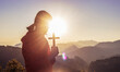 © AungMyo - Girl praying and holding Christian cross for worshipping God on mountain at sunrise background. Christian, Christianity, Religion copy space background. Easter Sunday concept: