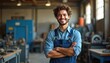 © Maryna - Smiling man in blue overalls stands with arms crossed in a workshop setting. He looks confident and happy. Industrial background with machinery visible.
