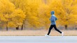 © Дмитрий Баронин - Jogger in blue hoodie and black pants runs along a path surrounded by vibrant yellow trees, showcasing an active lifestyle in a serene autumn landscape with copy space
