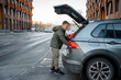 © KseniaJoyg - A man in a jacket is looking for something in the open trunk of a car outside in the cold season