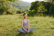 © SHOTPRIME STUDIO - Serene young woman practicing yoga outdoors in a green landscape, wearing gray athletic clothing and exuding tranquility, suitable for wellness and fitness themes