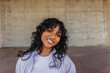 © PintoArt - Smiling young woman with curly hair against concrete wall