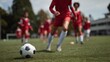 © ryker - Young soccer player running toward black and white ball on grass field during practice with teammates in red uniform training in blurred background, energetic and focused sports action