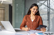 © Liubomir - Young indian accountant working on documents and using a calculator at her office desk. Managing financial data with a focused yet cheerful expression. Representing successful business and accounting