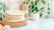 © sommersby - Artisan homemade flatbreads stacked on rustic wooden cutting board with flour on light blue table, surrounded by fresh greenery in bright, inviting kitchen