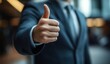© wilson - Close up of a businessman showing thumbs up gesture in an office building wearing business suit with blurred background