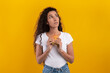 © Prostock-studio - A young woman stands against a bright orange yellow background, holding a burger in her hands. She looks up pensively, debating whether to indulge in the unhealthy food.