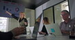 © Marco - Businesswoman gesturing toward screen while presenting to engaged team of professionals in conference room with laptops and windows