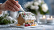 ©  VladaToday - Adult hands decorating gingerbread house with icing and candied fruits on blue counter at home