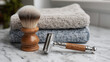 © Алексей Иванченко - Classic metal safety razor with wooden shaving brush and folded towels on marble bathroom countertop
