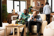 © DC Studio - Young diverse men seated on sofa with wireless controllers, playing video games on television in cozy living room. Multiethnic group of friends having gaming hangout in apartment.