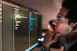 © artitwpd - Focused man in glasses analyzes code on a computer monitor in a modern office, representing software development, programming concentration, and tech-driven problem-solving in a digital workspace.