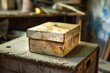 © nsit0108 - Dusty old cardboard box resting on wooden crate in a cluttered workshop, conveying a sense of age and disuse