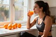 © Worldwide - Weight loss fitness nutrition diet. Woman enjoying orange juice by the window with fresh oranges nearby.