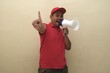 © Ahmad - Southeast Asian man in red shirt and cap shouting into megaphone while holding up fingers to count one isolated with copy space.