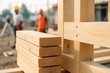 © hobonski - Smooth timber beams lie neatly stacked in the foreground while workers assemble a wooden frame behind them, showing progress, structure, and early construction stages.