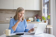 © Liubomir - Mature woman analyzing financial documents and bills, calculating expenses at her kitchen table while using a laptop for budgeting and planning retirement savings