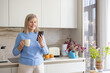 © Liubomir - Senior woman is standing in a modern kitchen, smiling while holding a mug and scrolling on her smartphone, embracing technology for communication and relaxation in her home lifestyle