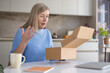 © Liubomir - Woman unboxing a brown cardboard package at a kitchen table, looking surprised and upset about the delivered contents, a concept representing online shopping issues and customer dissatisfaction