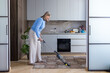 © Liubomir - Senior woman vacuuming carpet in a modern kitchen, smiling as she maintains a clean home, engaged in everyday domestic chores and enjoying active, comfortable retirement routine