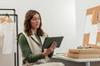 © Wavebreak Media - Woman reviewing tablet at fashion design studio desk with packaging boxes, markers and corkboard