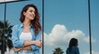 © Vasiliy - Confident smiling young woman standing outdoors in the city. Happy female professional in casual attire in front of a modern building with sky reflection