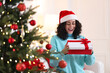 © New Africa - Happy woman with Santa hat and gift near Christmas tree at home