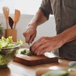 © Thanachart - Hands chopping fresh herbs on a wooden cutting board beside a salad bowl