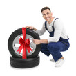 © New Africa - Tire service worker and car wheel with red ribbon bow on white background. Special offer or discount