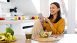 © Home-stock - Positive young lady eating fresh salad and using cellphone, sitting at table in kitchen while having healthy dinner, copy space