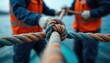 © Maryna - Two crew members in orange vests tie boat rope tightly. Work together on ship deck, ensuring safety. Strong knot secures marine line. Sailors moor large vessel with teamwork, showing collaboration,
