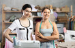 © JackF - Two smiling young professional seamstresses in casual clothing standing in fashion workshop, taking break from sewing and custom garment making..
