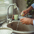 © Miljan Živković - Man washing glass under running water in kitchen sink