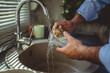 © Miljan Živković - Man washing glass under running water in kitchen sink